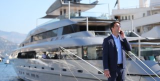 Yacht broker in a suit standing on marina talking on the phone in front of a luxury yacht